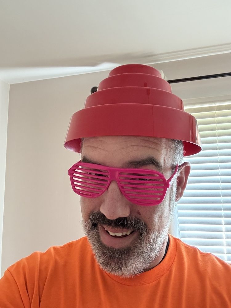 Seth dressed in bright orange shirt, pink shutter glasses and a Devo band hat