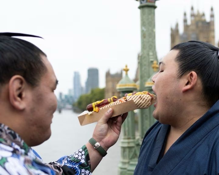 Yokozuna Hoshoryu feeding a hot dog to Yokozuna Onosato in London