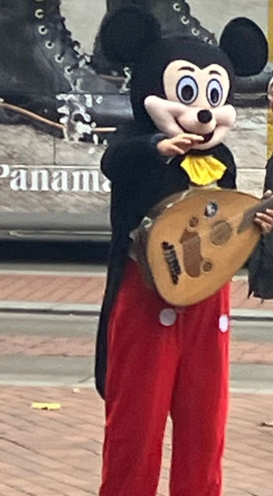 Ein Straßenmusiker mit Mandoline und einem Micky Maus Ganzkörperkostüm