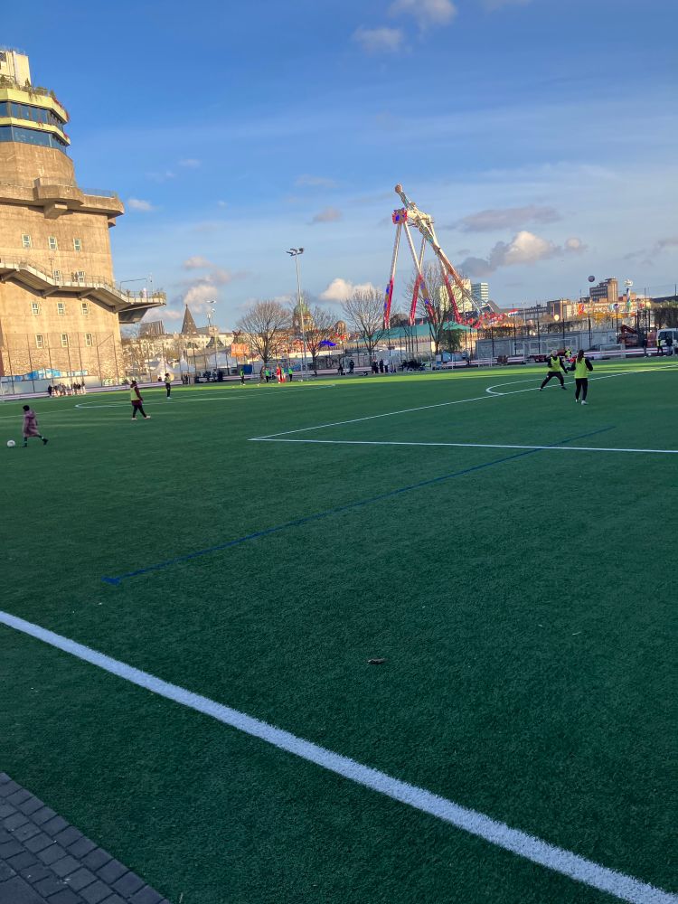 Ein Kunstrasen und m Hintergrund Fahrgeschäfte auf dem Dom und ein alter Hochbunker