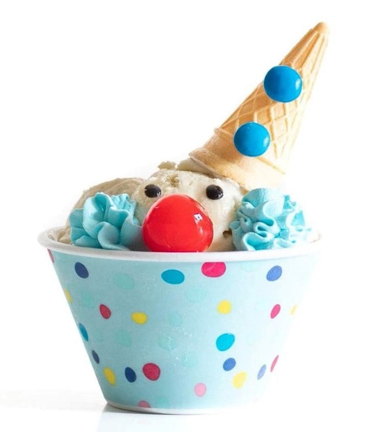 A paper ice cream bowl that has light blue background with polka dots, with ice cream peaking out of the bowl that looks like a clown