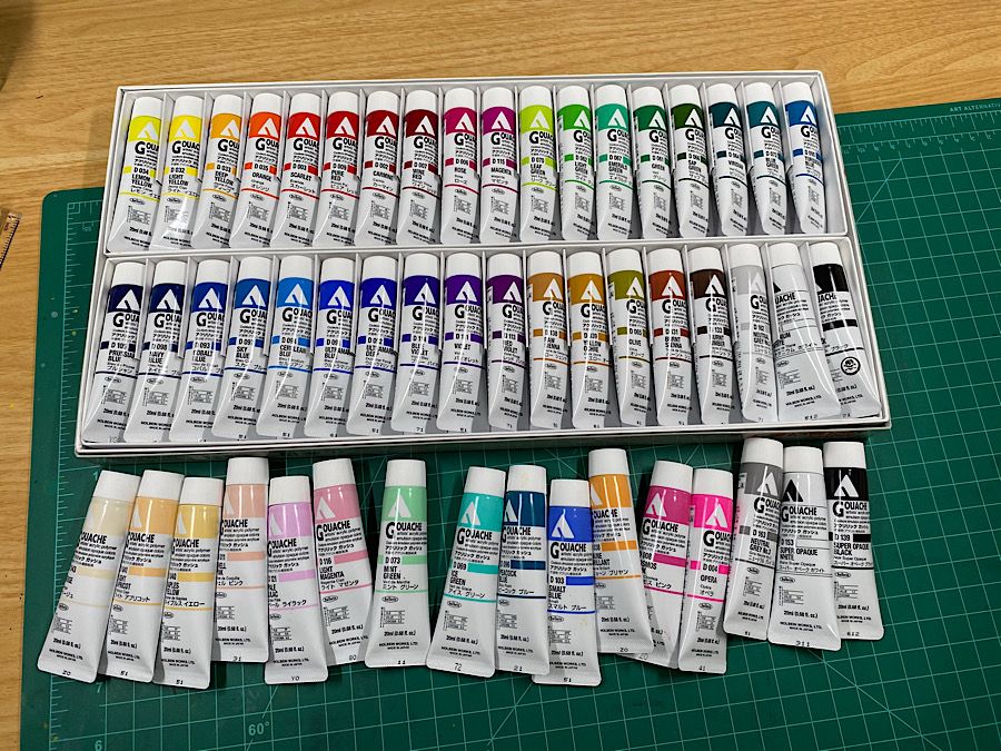 Photo of many tubes of Holbein acryla gouache. Some are loose and some are in a box.