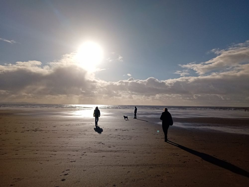 A beach with sea and sun bursting through cloud.
