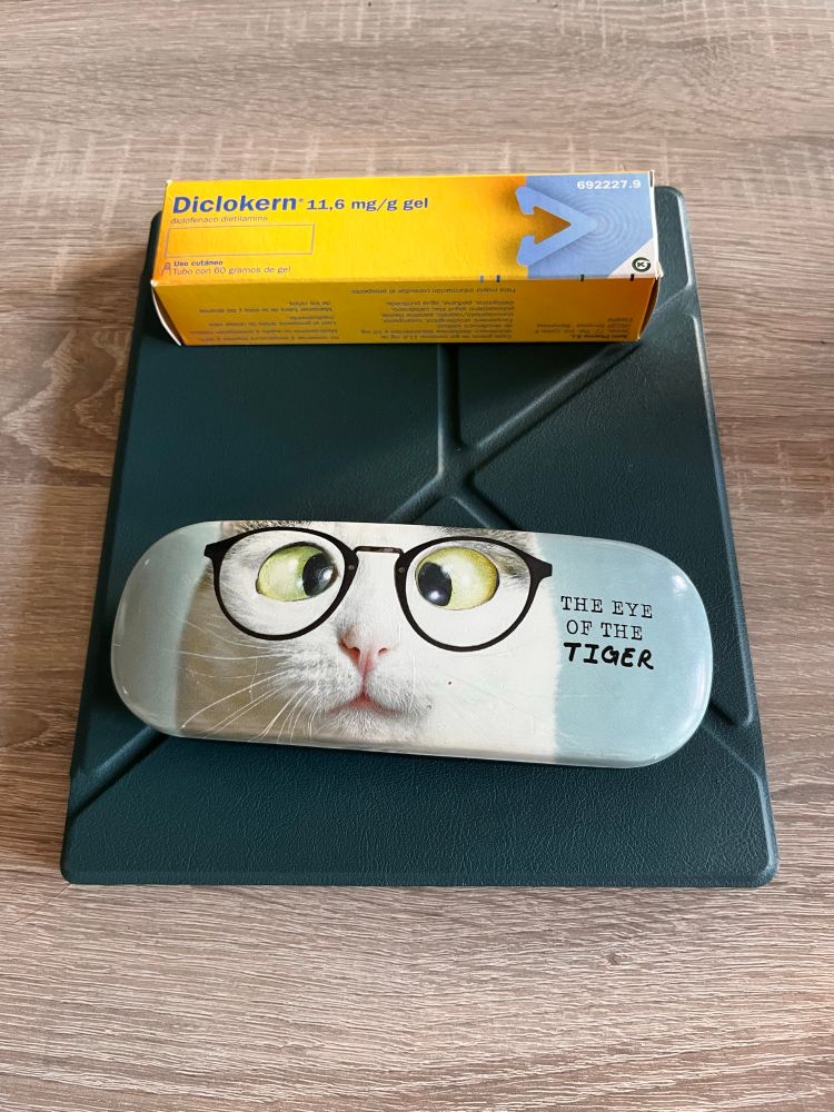 Foto de una funda de gafas, un lector de libros electrónicos grande y una caja de diclokern (el voltaren genérico)