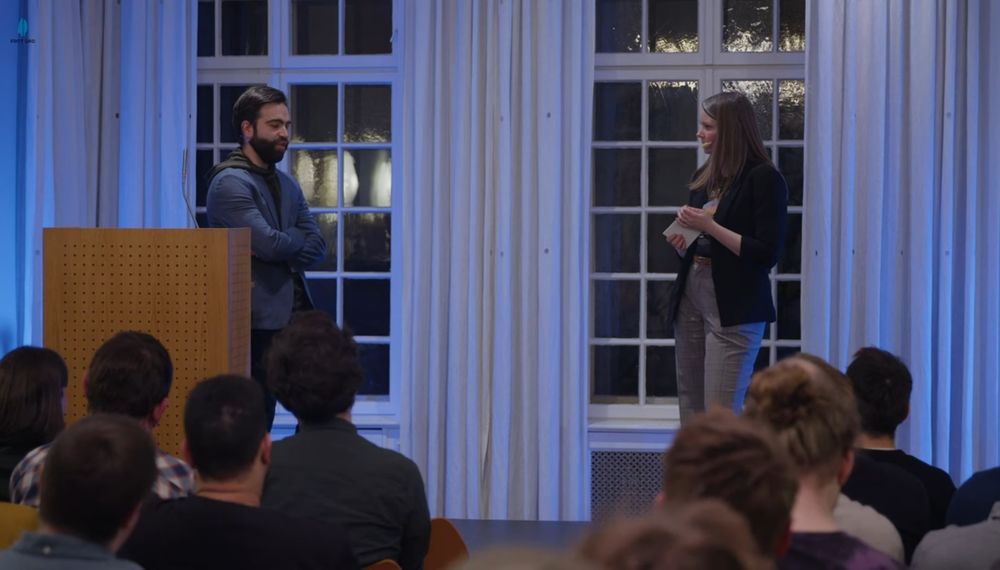 Jacob Geller and Frida Danmo standing on stage talking inn front of an audience.