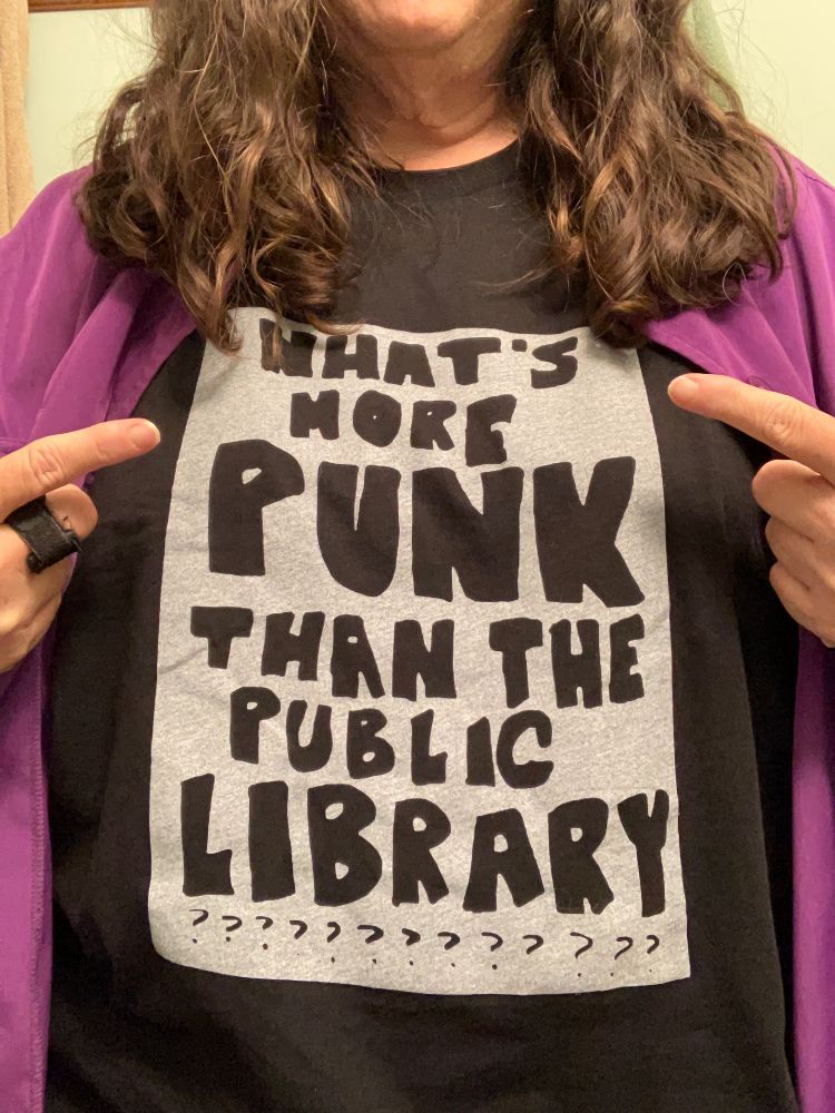 the torso of a person wearing a black t-shirt that says "What's more punk than the public library?”