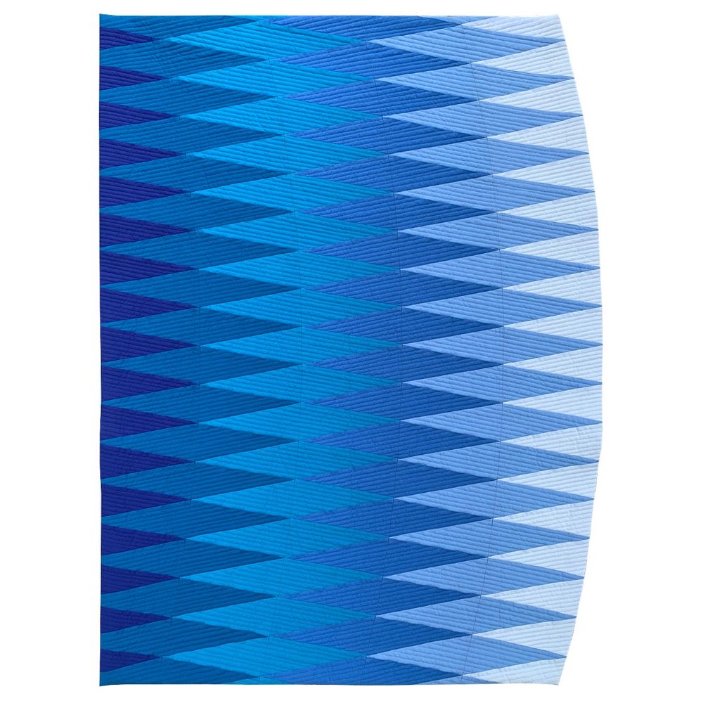 Description: Inspired by traditional diamond one-patch blocks, this design embraces the diamond shape while drawing it into a curved form to evoke feelings of a growing wave. The pairing of a soothing blue and turquoise color palette with an energetic diamond motif develops an ebb and flow, echoing the underlying energy of a calm ocean.