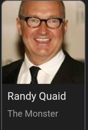 Actor Randy Quaid smiling in glasses and a suit and tie billed as The Monster
