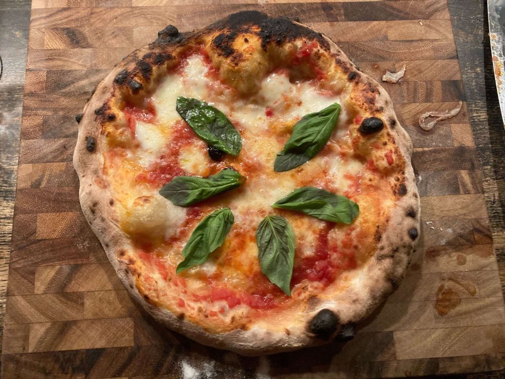 A margherita pizza with six basil leaves and a crust that is overly charred in some locations