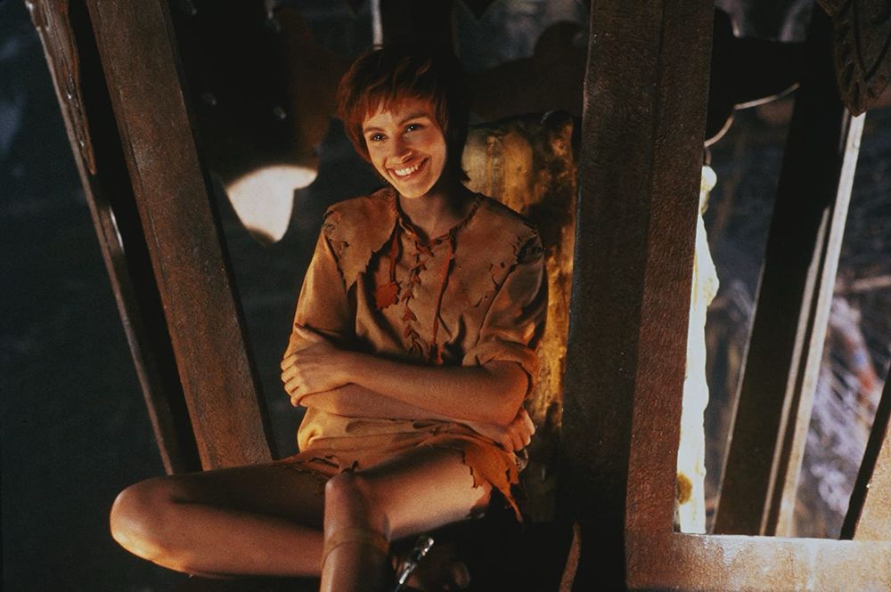 Julia Roberts dressed as Tinkerbell wearing a brown shirt, orange skirt and sitting in a lantern. 