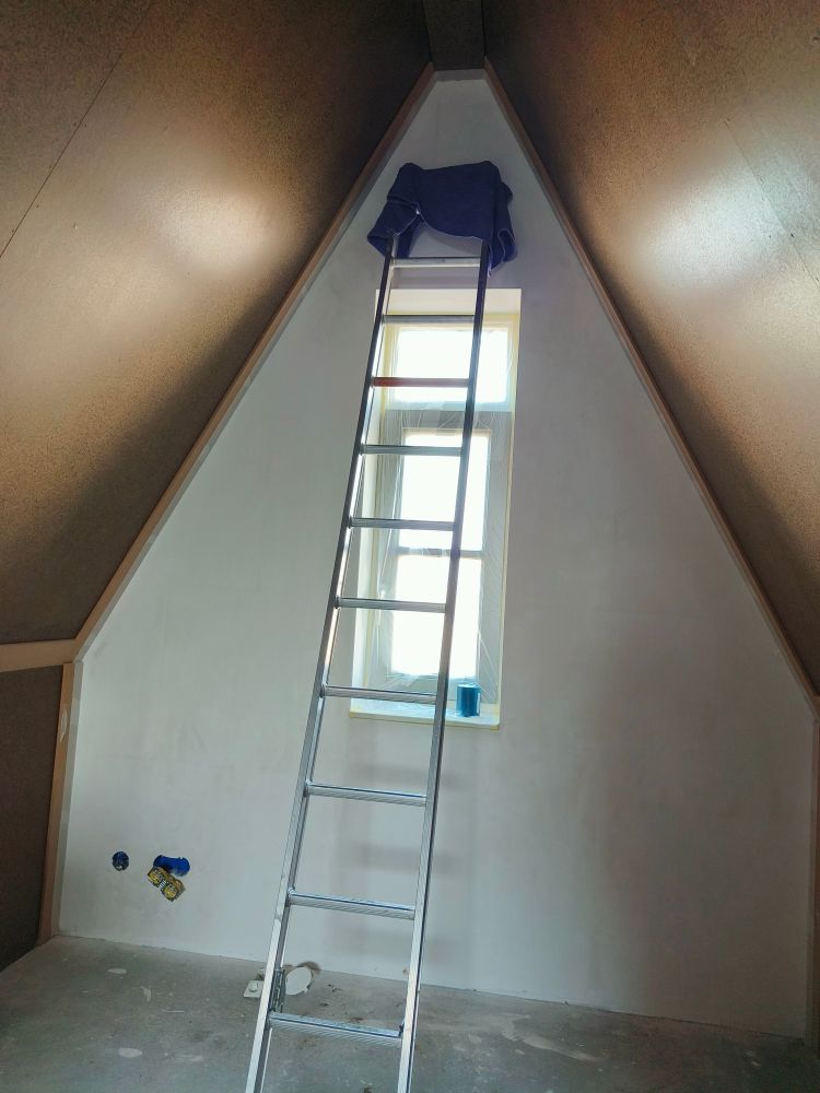 A photo of the second floor. The roof is slanted on both sides and there's a ladder leaning against the wall that has a small window on it to reach the high point.
I got fucking terrified on that ladder but I did tape it up!!! 