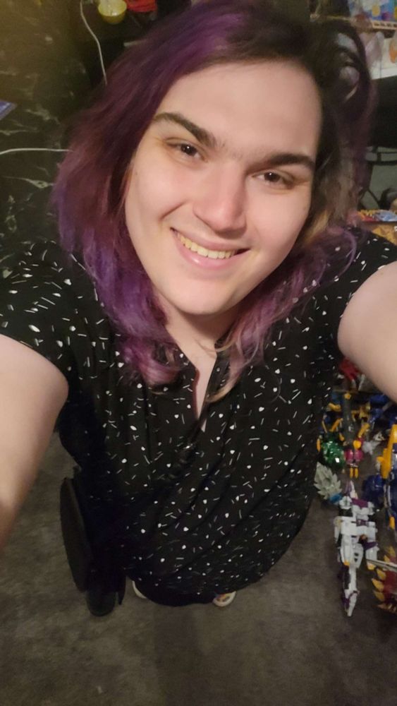 Fable, a white enby with purple hair, smiling showing off their black blouse