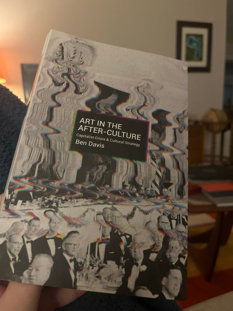 The book Art in the After-Culture by Ben Davis, held in front of a living room scene. 