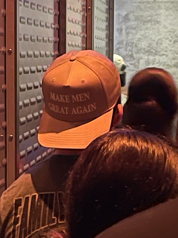 Person wearing silver-ish brown baseball hat backward. Hat has the words: "Make Men Great Again" stitched on the front.