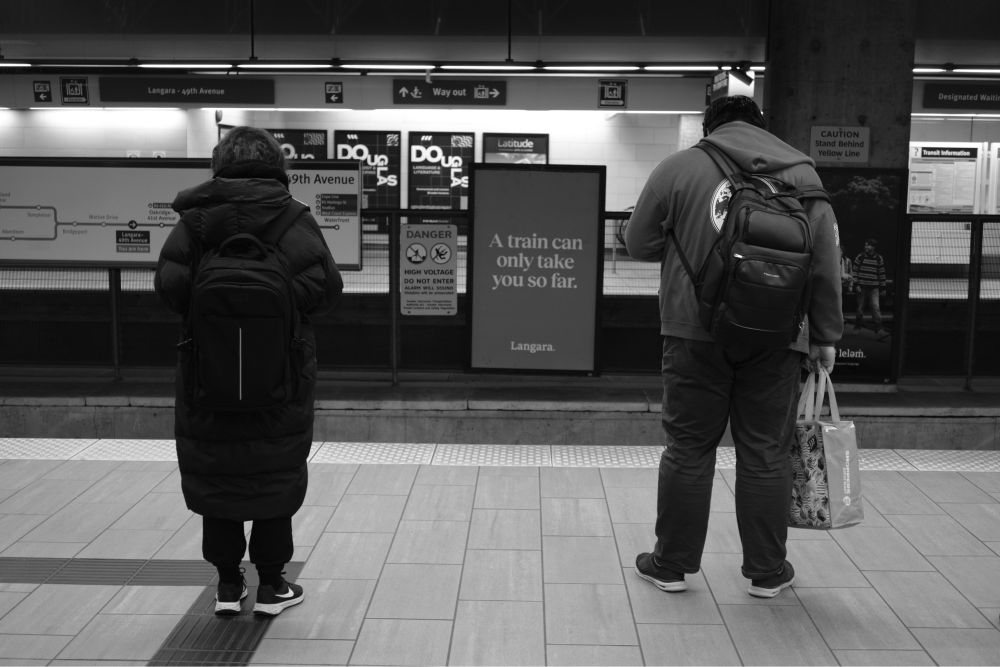 Two people patiently wait for a train to arrive in an underground train station. It is very quiet, as they are the only two people waiting on the platform.