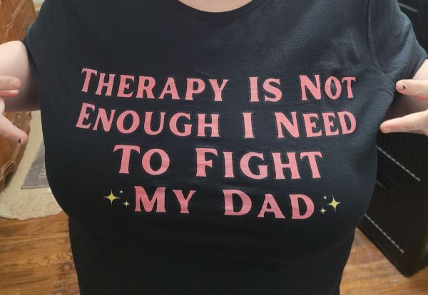 OP wearing a black t-shirt and pointing to it. The shirt has red text that reads, "THERAPY IS NOT ENOUGH I NEED TO FIGHT ✨ MY DAD ✨"