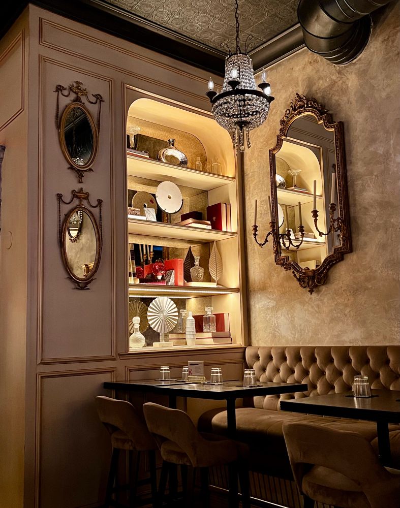 Beautiful corner in restaurant with a booth, mirrors on wall and bookshelf that’s decorated with ornate object