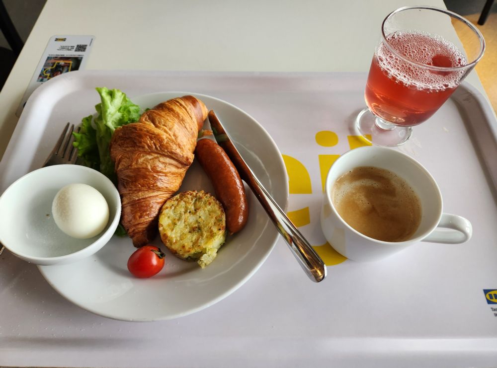 イケア立川店　モーニングセット　クロワッサン、ゆで卵、レタス、トマト、太いソーセージ、野菜のメダリオン（ダイス状のじゃがいも等を小さい円盤状にまとめて焼いたもののようだ）のプレート　ホットのカフェオレ　リンゴンベリードリンク