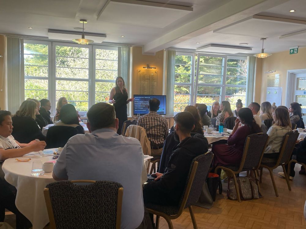 A photograph taken during the event. The room is filled with members of staff from various regional healthcare organisations. They are listening to a paediatric doctor deliver a presentation.