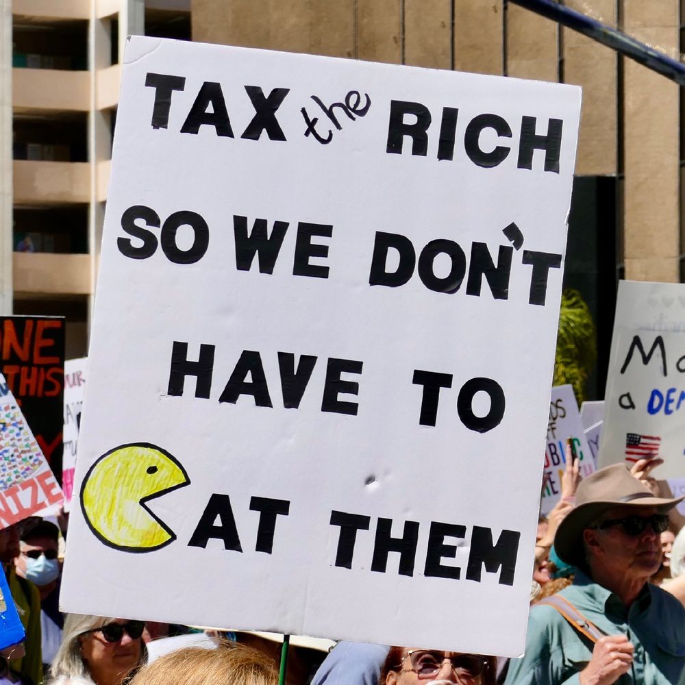 Protestor sign reads — Tax the rich so we don’t need to eat them. 