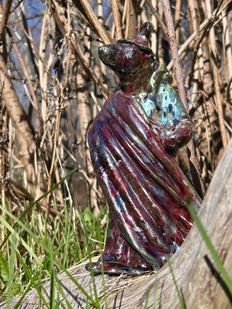 A photo of the sculpture outside where you can see branches and grass. 