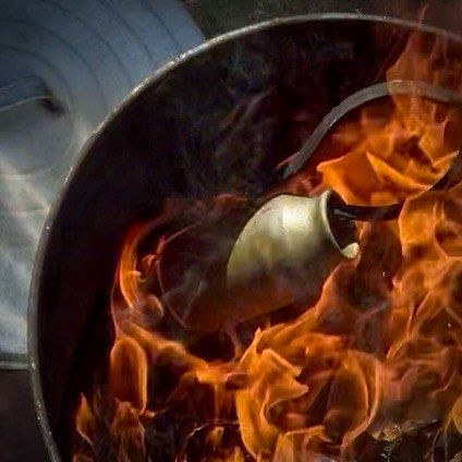 A raku-vase being placed into the raku reduction container while flames encompass it.