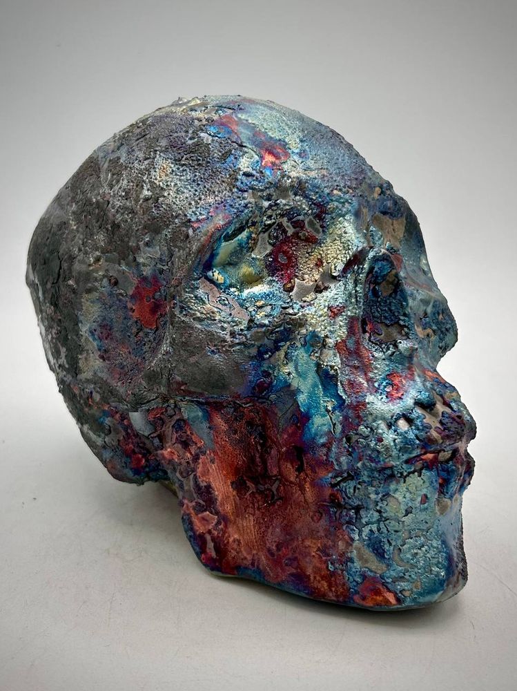 A raku skull with glazes in red, purple, blue and charcoal black. View of right side of face.