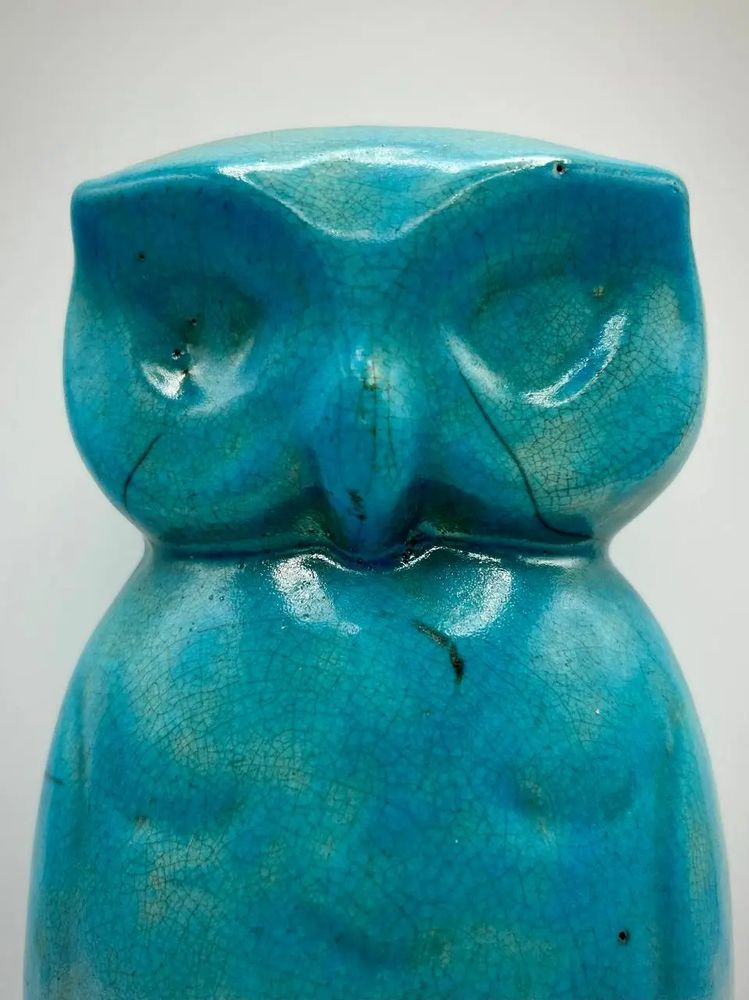 A closeup of the face of a turquoise ceramic owl with the distinctive black cracks and lines from the raku pottery process