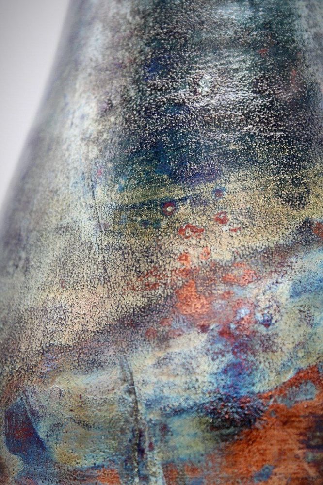 A closeup shot of the neck of raku pottery vase Starlight Nebula with deep blues, oranges, reds and greens.