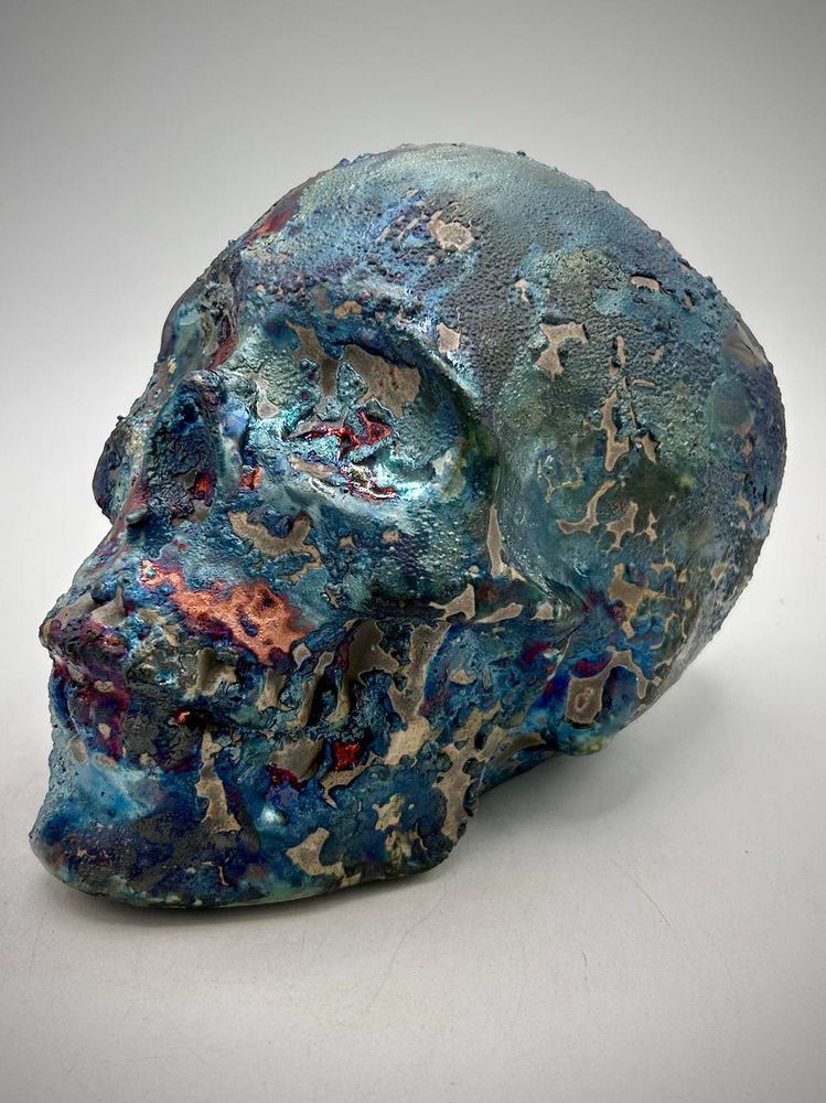 A raku skull with glazes in red, purple, blue and charcoal black. View of left side of face.
