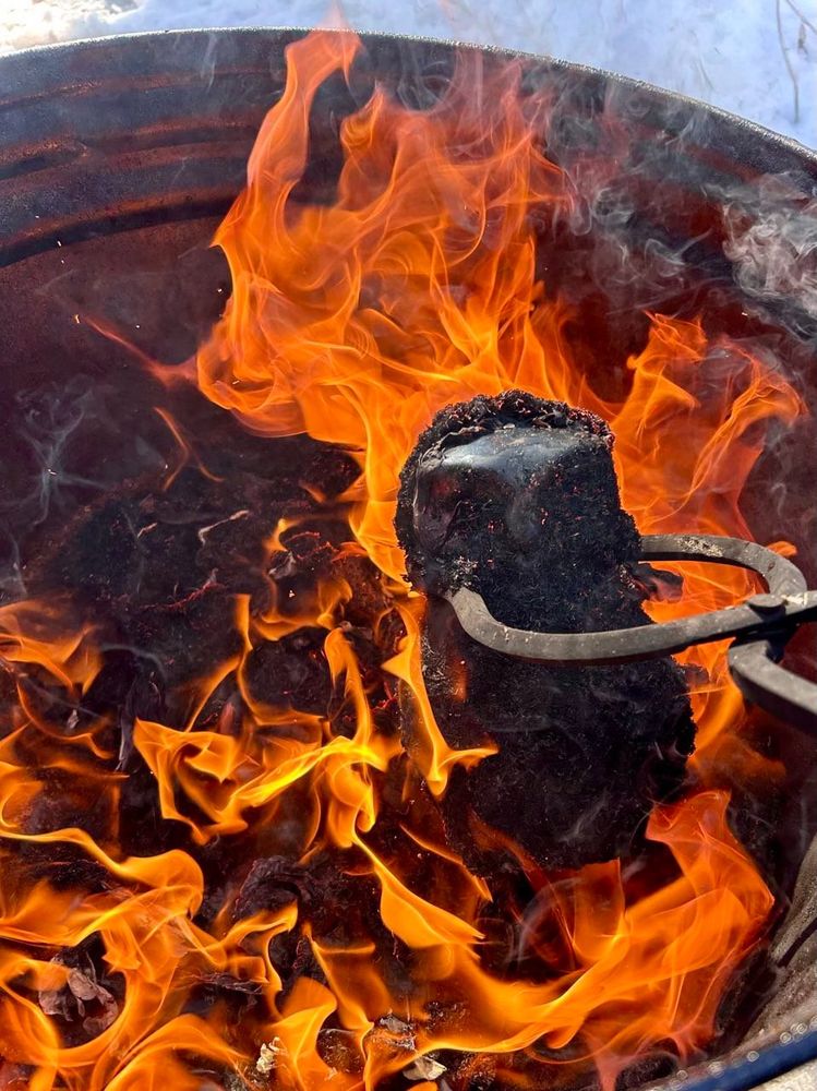 A raku fired ceramic owl being placed from the kiln and into the reduction container with flames surrounding it
