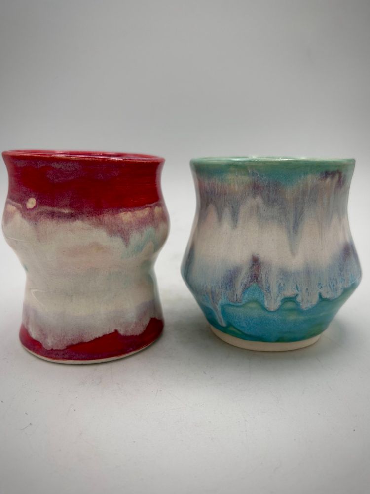 Two porcelain tumblers with melty looking glazes.  The first is white with reds and pinks.  The second has turquoise, white and purples. 