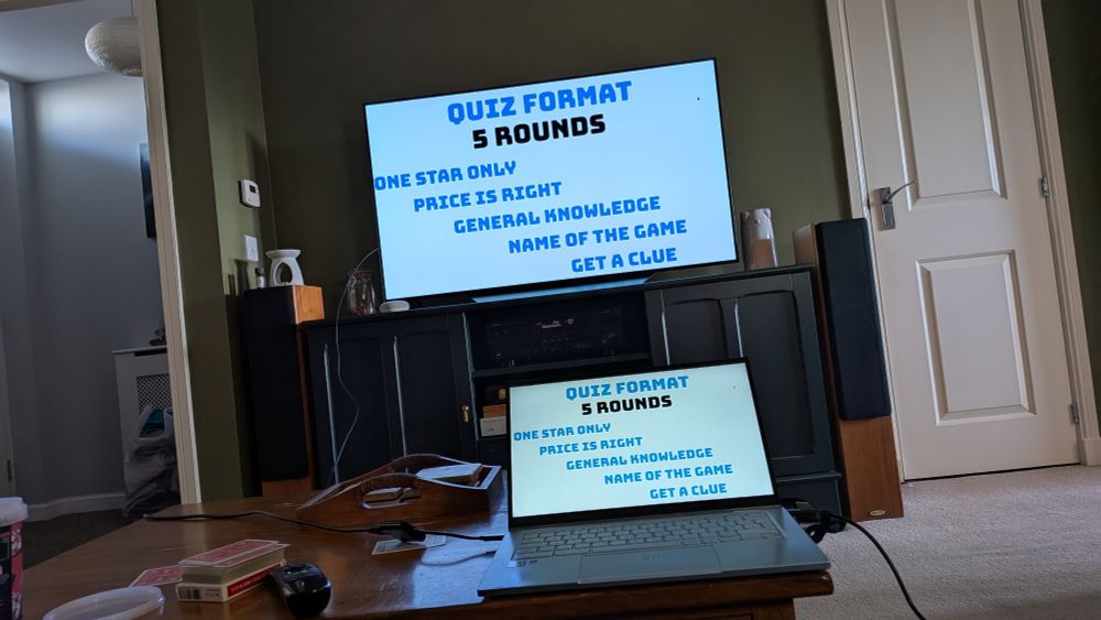 Computer on a table showing the quiz rounds and the TV behind it mirroring the screen. 