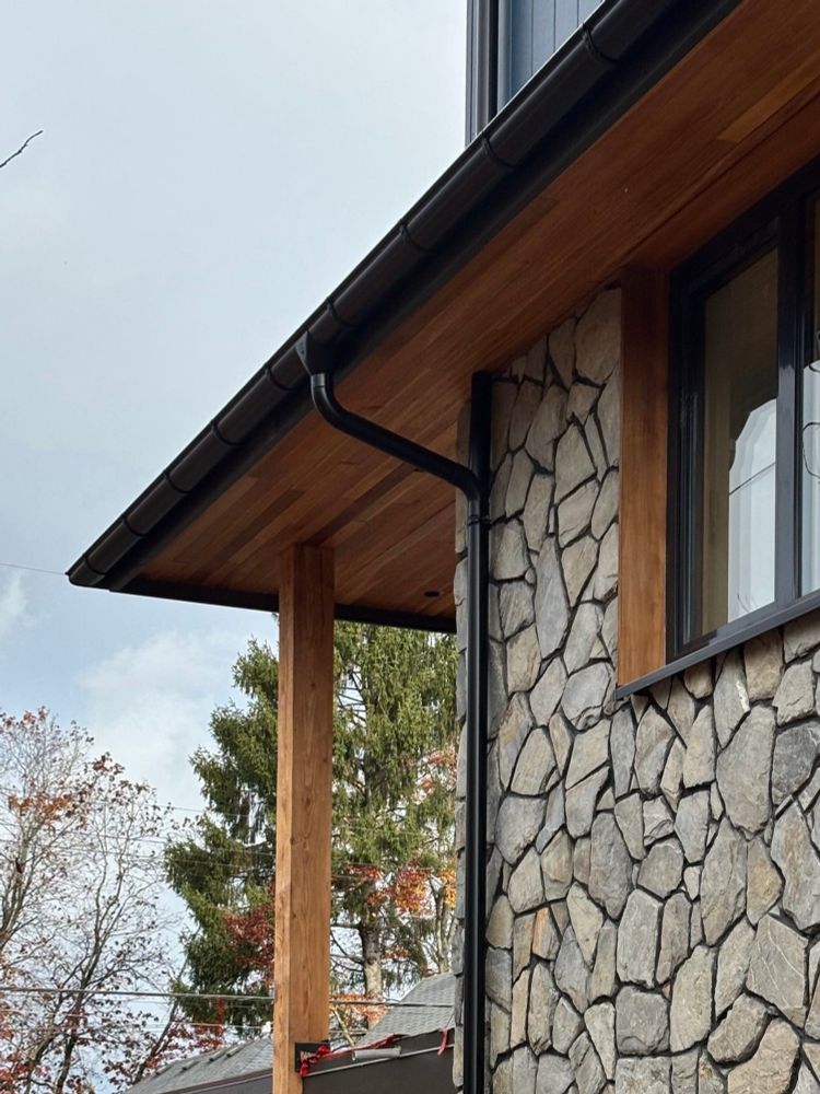 House with stone clad wall and cedar soffit, with black gutter and downspout 