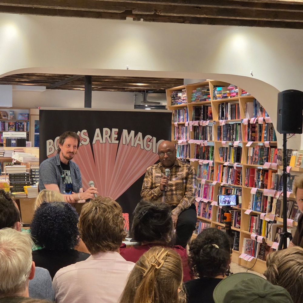 Nat and Maurice sitting in front of the Books Are Magic backdrop in front of a full house audience 