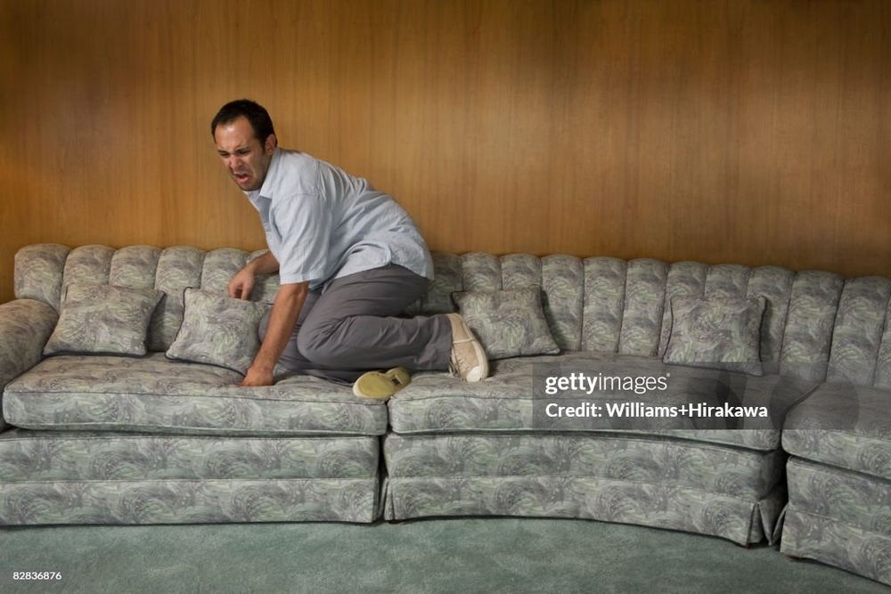 A man on a couch has feet up on a coach and looks frightened.