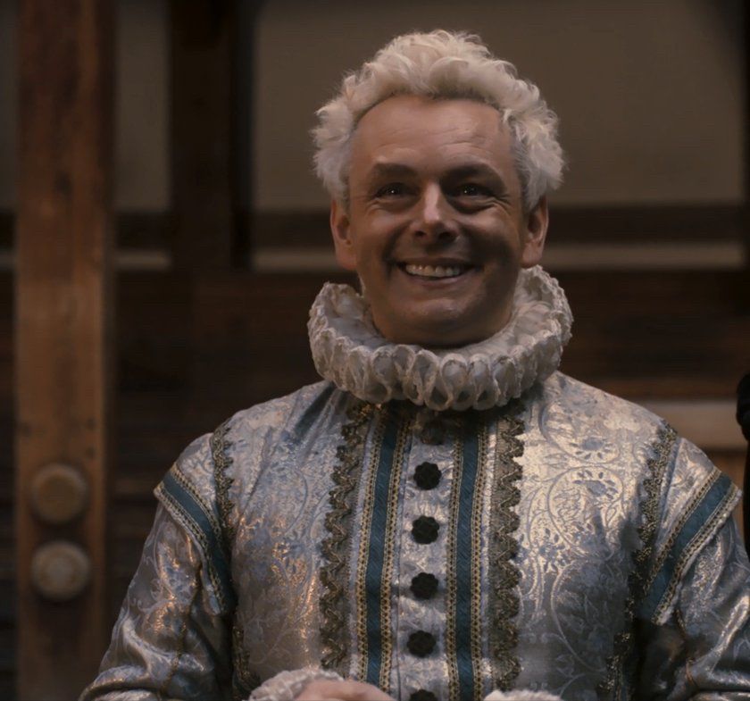 Michael Sheen as Aziraphale in Good Omens in the Shakespeare Globe scene. His hair is light blonde and fluffy and he is smiling widely. 