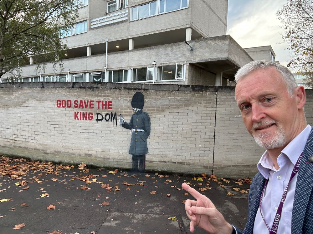 Cllr Mark Wilson pointing to a new suspected Banksy in Windsor reading God save the king with a soldier adding dom to read god save the kingdom 
