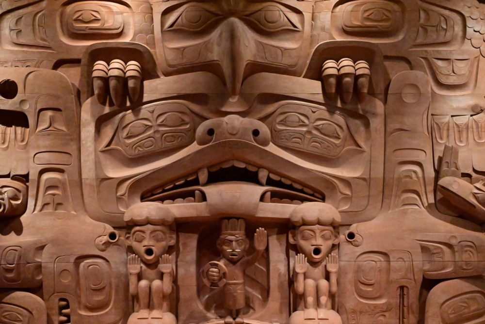 A large wall artwork, depicting many human and mythic forms characteristic of the Pacific Northwest.  