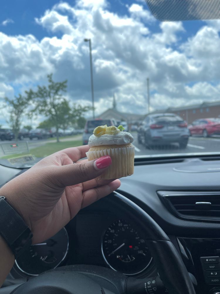 Tanesha holding a vanilla cupcake that was absolutely delicious in her car. In the background, you can see her church and a beautiful cloudy sky.