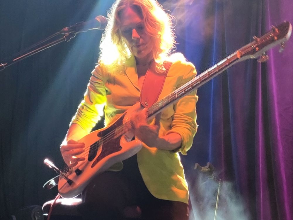 Britta Phillips on stage at the Trades wearing a bright yellow jacket 