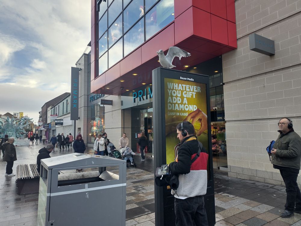 Tim holding his microphone against an electronic advertising screen. There is a seagull on top of the screen just taking off