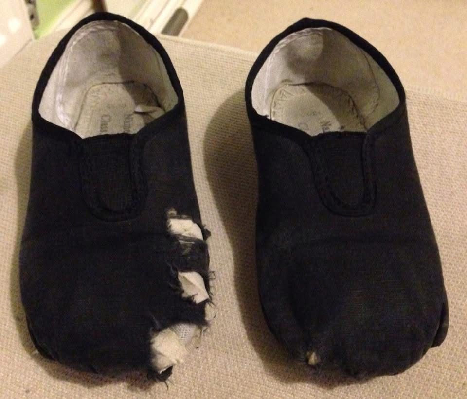 Child’s black gym shoes in embarrassingly worn state including numerous holes. 