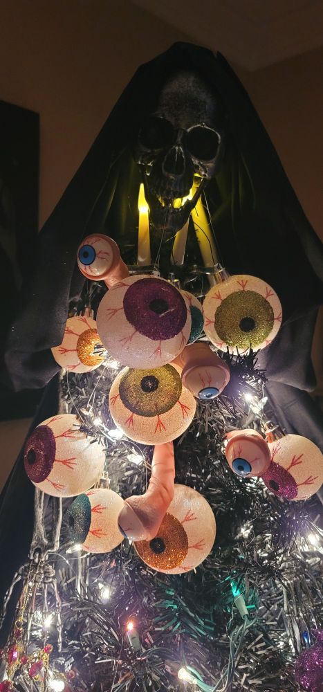 Closeup of a tree topper made from a small skeleteon, a cluster of eyes bursting from its ribcage, and a hooded cloak draped over the skull.
