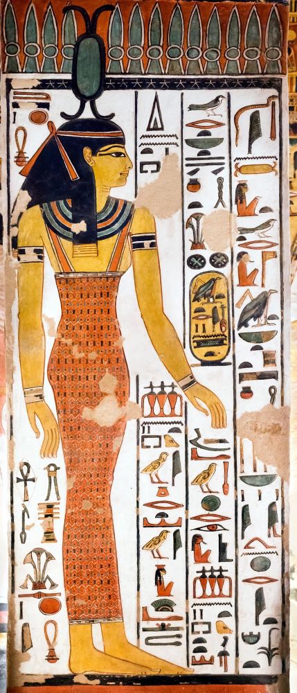 Ancient Egyptian depiction of the goddess Neith.  She is wearing a long flowing dress and upon her head is her symbol of two arrows crossed with a green shield.