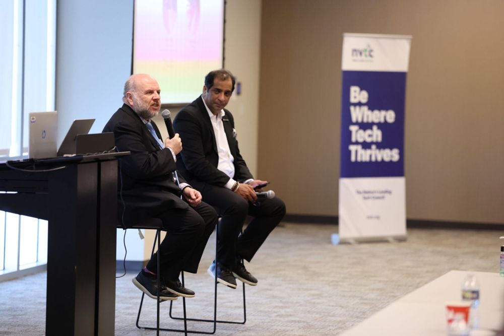 Buddy Rizer and Vinay Nagpal during their Fireside Chat, and in the background a pull-up banner that says "NVTC. Be Where Tech Thrives"
