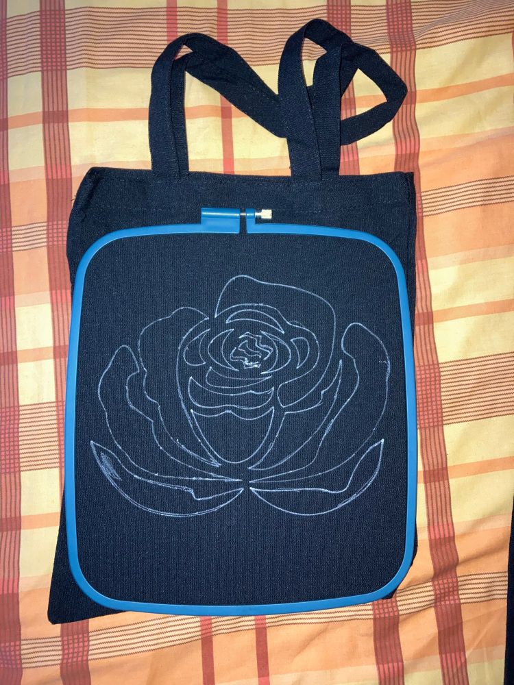 Bolsa negra de lona con bastidor alrededor y flor dibujada en el centro.