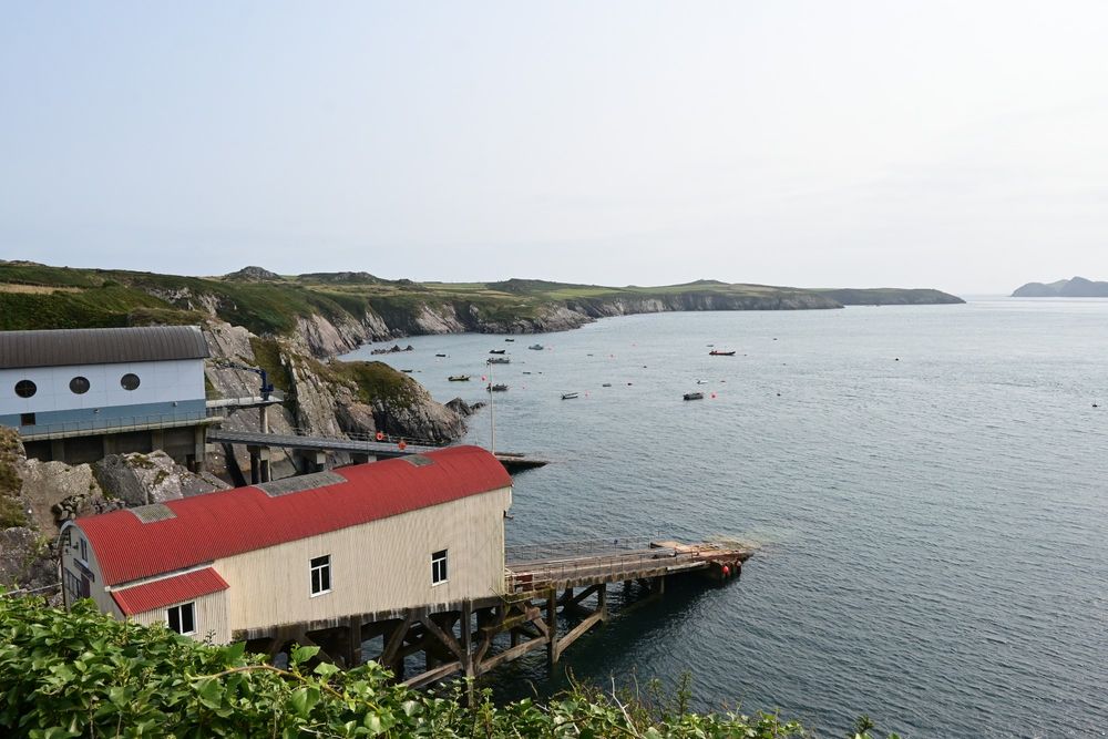 Two metal buildings with slipways to the sea. On long coastline with the sea to the right 