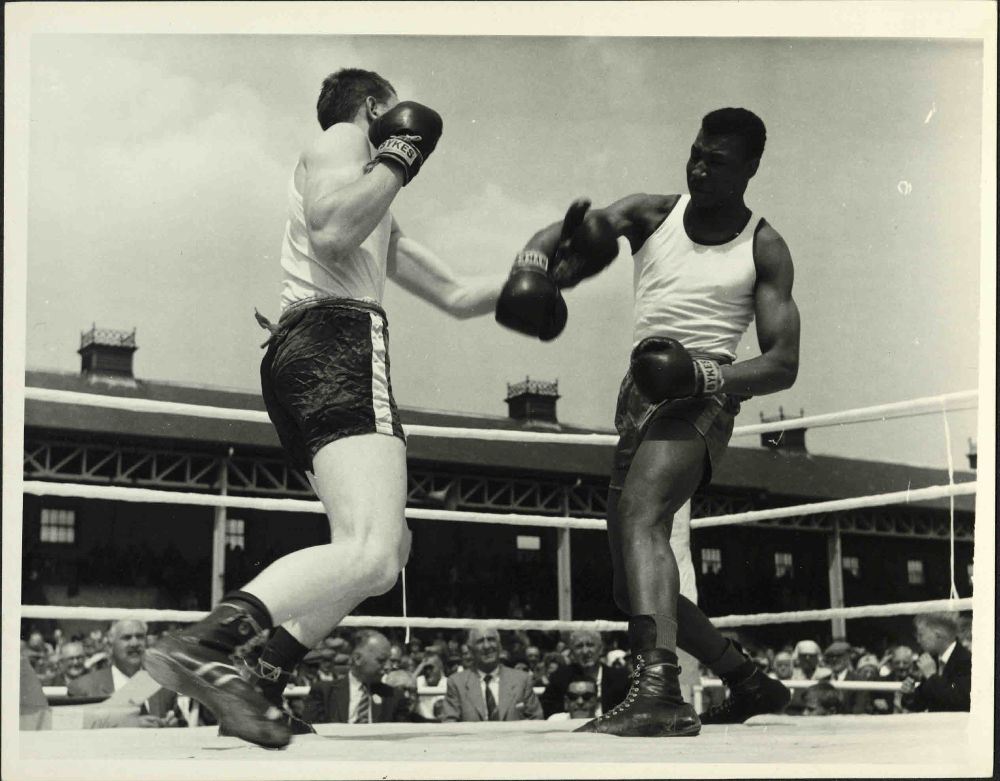 Photograph of competitors in a boxing match at 1963 Yorkshire Miners' Annual Demonstration, held in Doncaster. The boxing ring is outside, with a large crowd watching. 