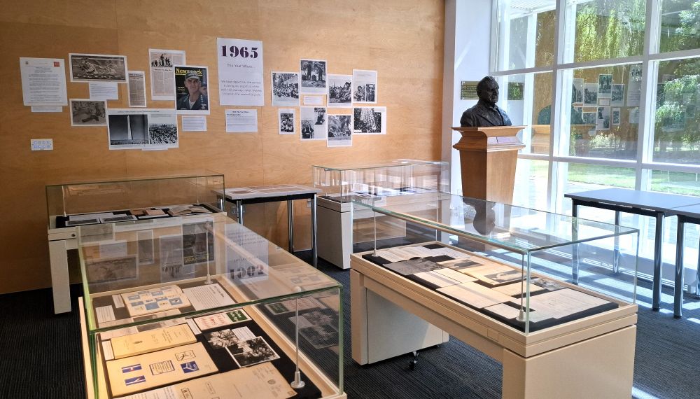 Photograph of the Modern Records Centre exhbition space featuring cabinets full of archive material and a poster advertising 1965 on the wall.